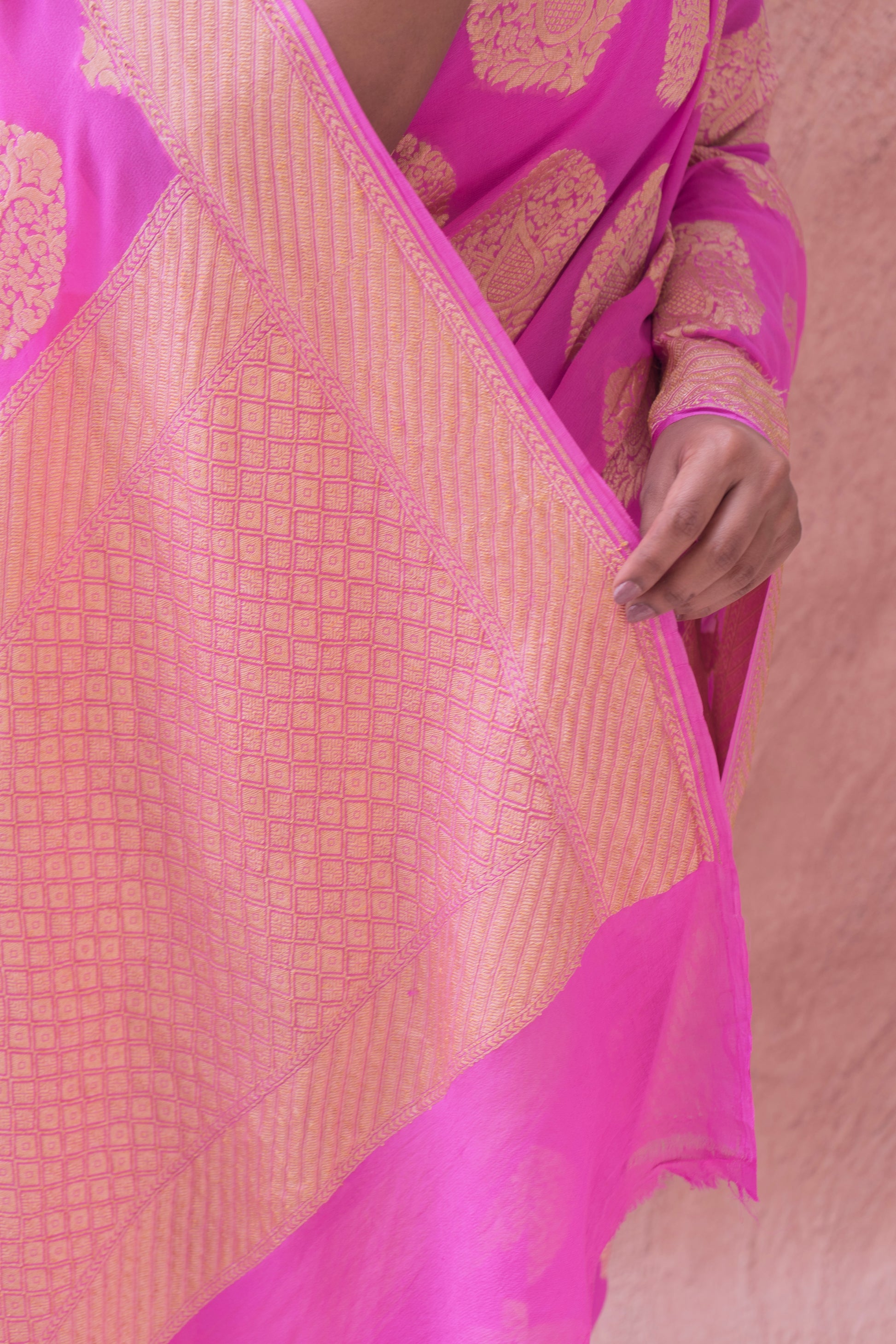 A stunning pink Banarasi saree adorned with gold patterns, showcased on a neutral background 