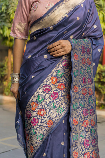 A person showcases a blue Banarasi saree with floral patterns and zari borders, paired with a contrasting pink blouse piece