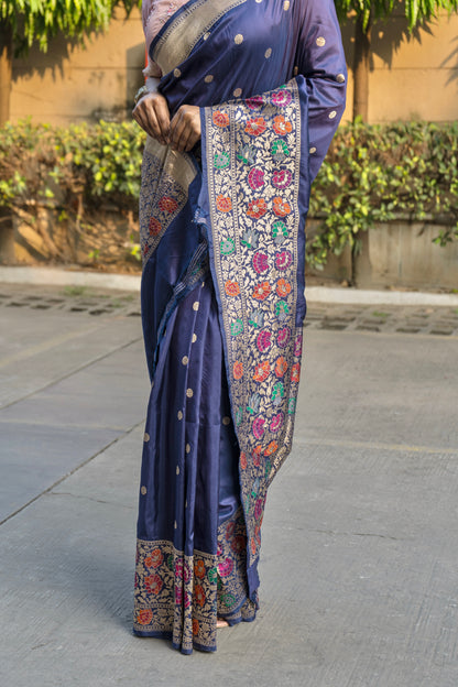 A stunning blue Banarasi saree featuring floral designs and zari detailing, complemented by a pink blouse piece.