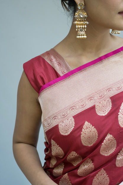 A maroon Banarasi saree with delicate white patterns, showcased beautifully against a soft grey background