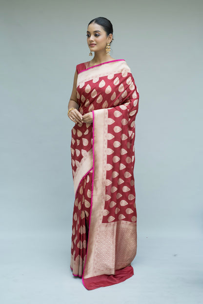 Exquisite maroon Banarasi drape with white detailing, made to shine against a grey background.