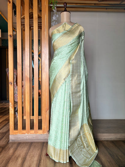 A stunning light green Banarasi saree with golden detailing, presented on a mannequin in a neutral setting.