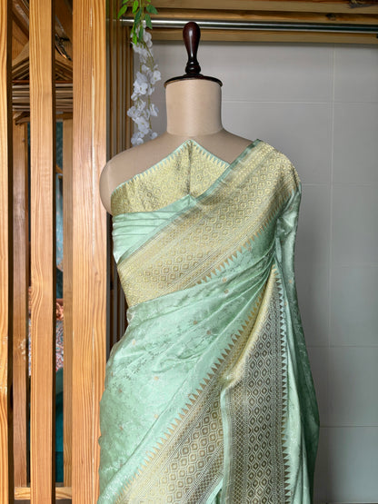 A light green Banarasi saree with intricate gold patterns displayed on a mannequin against a neutral background