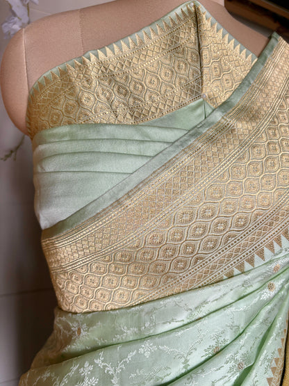 A stunning light green Banarasi  saree creation with gold designs, elegantly displayed on a mannequin on a neutral background.