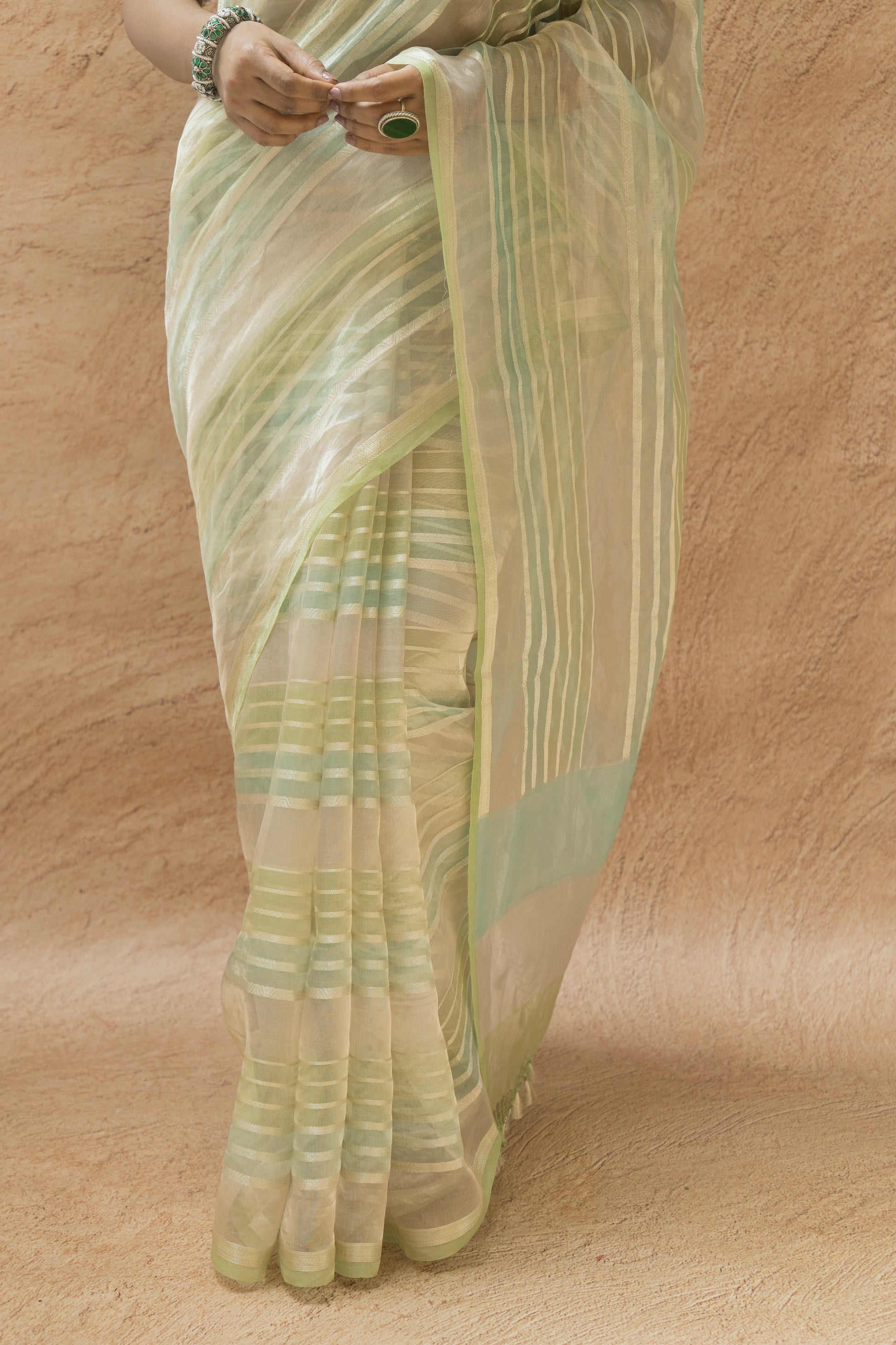 Model dressed in a light green luxury Banarasi saree featuring delicate patterns on a beige backdrop