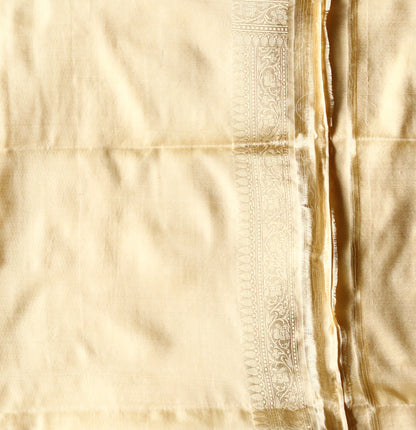 A woman in a light cream Banarasi saree with classic zari borders, radiating effortless sophistication.