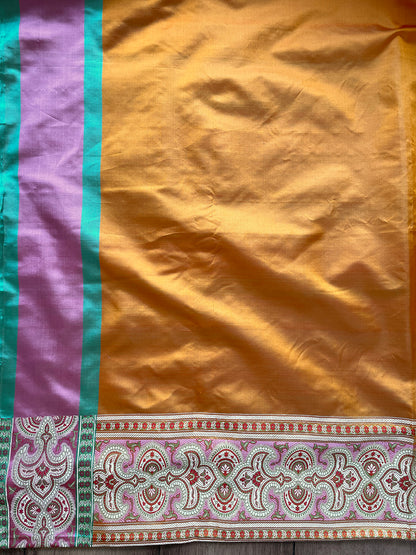 A graceful pose in a mustard yellow Banarasi saree featuring geometric patterns, floral designs, and a rich green-gold border.