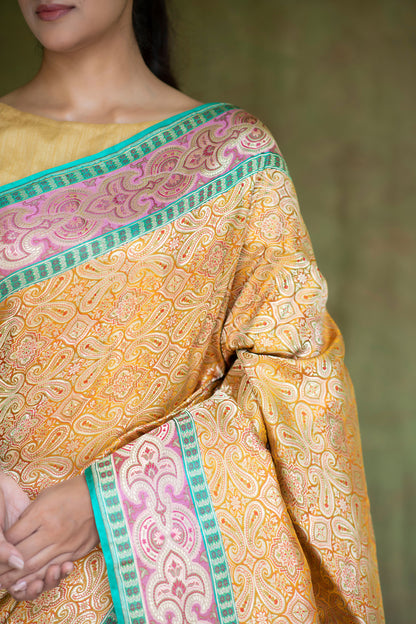A stunning mustard yellow Banarasi saree with geometric and floral designs, highlighted by a green-gold border.