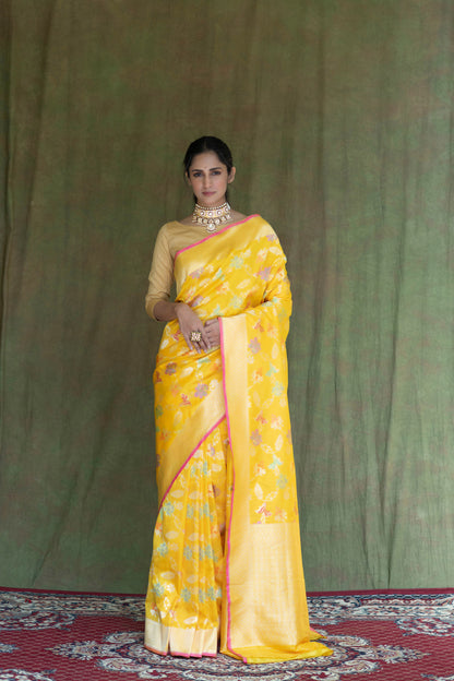 A stunning yellow Katan Multi-Meena Banarasi Silk Saree with floral design and zari accents, paired with a solid blouse piece