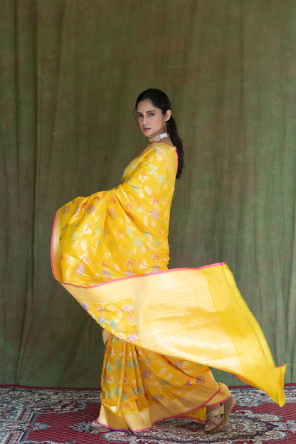 A woman showcases a yellow Katan Multi-Meena Banarasi Silk Saree with floral motifs, rich zari work, and a solid blouse piece.