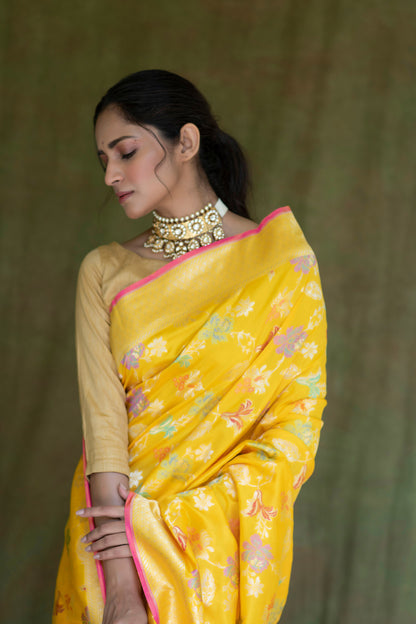 A woman draped in a yellow Katan Multi-Meena Banarasi Silk Saree with intricate floral artistry, zari detailing, and a solid blouse piece