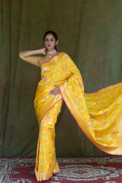 A woman radiates grace in a yellow Katan Multi-Meena Banarasi Silk Saree with floral patterns, zari embellishment, and a solid blouse piece.