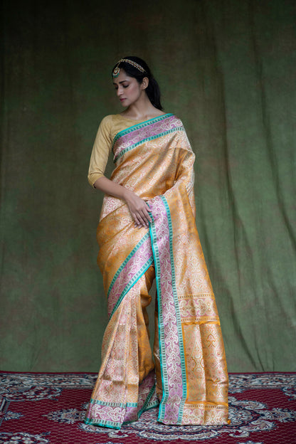 A woman adorned in a mustard yellow Banarasi saree with geometric work, floral artistry, and a striking green-gold border.