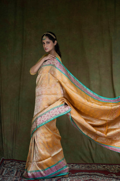 A woman radiates elegance in a mustard yellow Banarasi saree with geometric motifs, floral accents, and a green-gold border