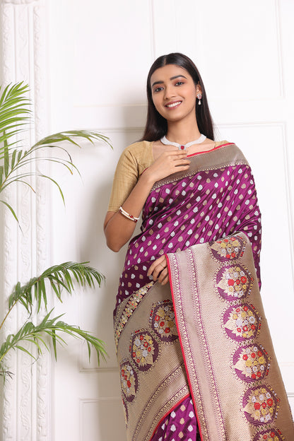 A woman poses gracefully in a purple Banarasi saree with intricate silver and gold patterns, zari work, and a contrasting red blouse piece
