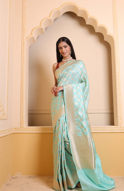 A woman in a sky-blue Booti Katan Upada saree with detailed zari work and a flowing leheriya pallu, styled with a separate blouse piece — pure Banarasi grace.
