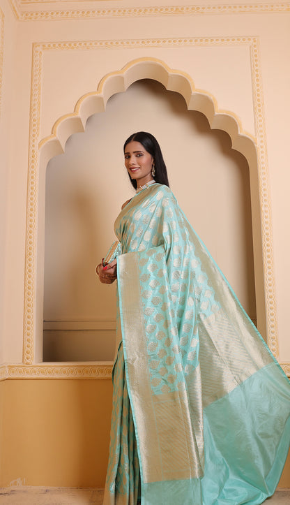 A woman wearing a sky-blue Booti Katan Upada saree with an intricate zari border and leheriya pallu, paired with a separate blouse piece — a timeless Banarasi saree elegance in one line.
